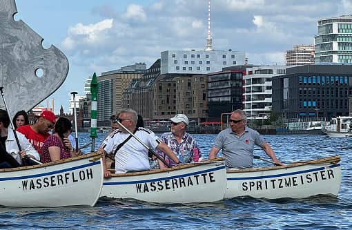 backstagetourism-teamevent-01 Nahaufnahme von drei Ruderbooten mit den Aufschriften „Wasserfloh“, „Wasserratte“ und „Spritzmeister“ – Teilnehmer genießen die Fahrt durch Berlin.