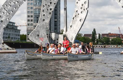 backstagetourism-teamevent-03 Drei Ruderboote mit fröhlichen Teilnehmern vor der monumentalen Skulptur “Molecule Man” auf der Spree in Berlin